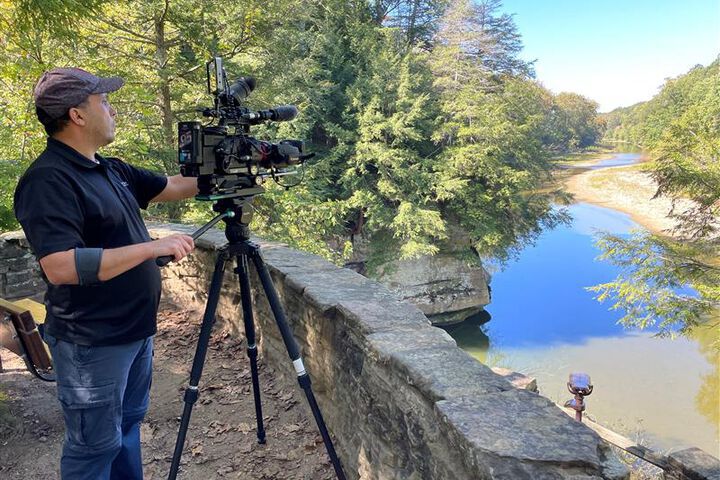 A male student uses a professional camera to film an outdoor scene.